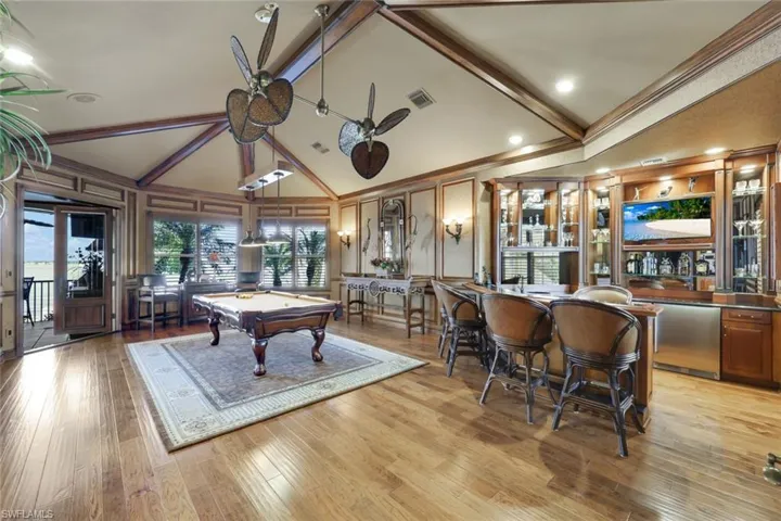 Billiards room with high vaulted ceiling, billiards with stunning views of the water, indoor bar, ceiling fan, and Hickory Hewn Floors. Copper sink and small fridge.  Opposite wall is a painting of a famous Golfer, Bobby Jones, a hand made painting surrounding him to complete the stunning visual.