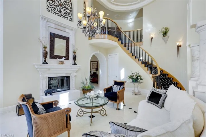Living room with marble Floors, Marble posts, a towering ceiling approx. 25 ft, ornamental molding, and an inviting chandelier.  French doors to the pool and private beach, double sided fireplace that has never been used
