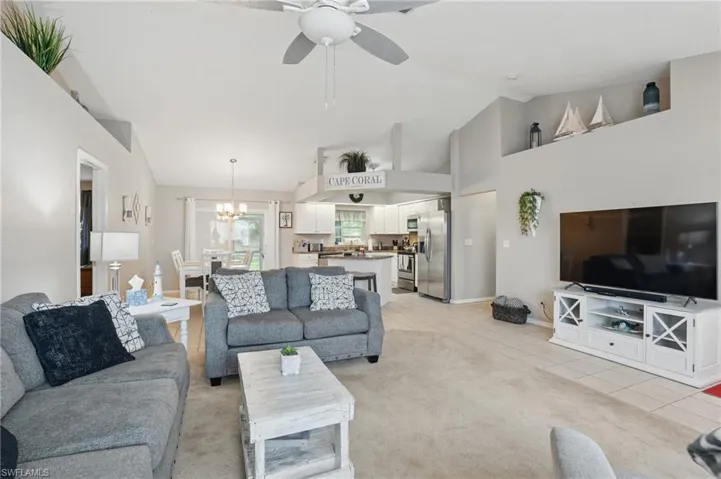 Living area with a chandelier, a ceiling fan, light carpet, light tile patterned flooring, and high vaulted ceiling