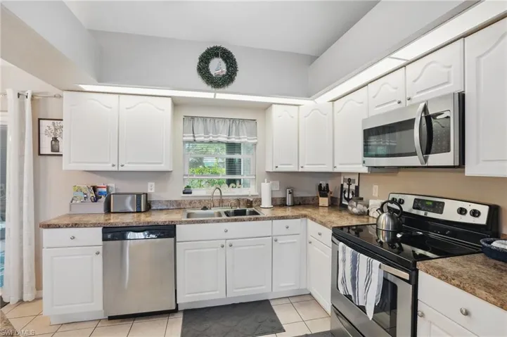 Kitchen with appliances with stainless steel finishes, a sink, light tile patterned flooring, and white cabinets