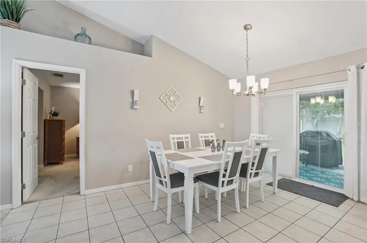Dining area with lofted ceiling, a chandelier, light tile patterned floors, and baseboards