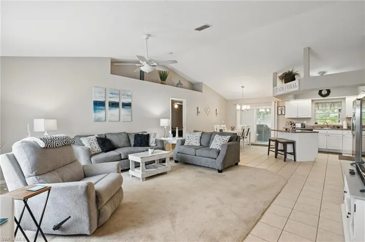 Living area featuring light tile patterned floors, a chandelier, high vaulted ceiling, and a ceiling fan