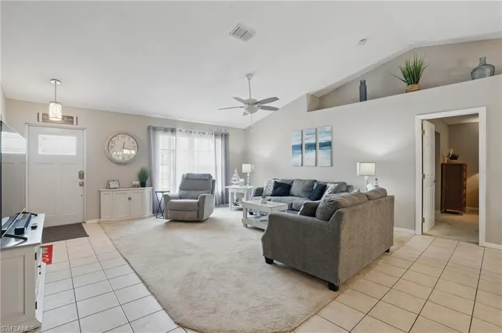 Living area with light tile patterned floors, light carpet, a ceiling fan, lofted ceiling, and baseboards