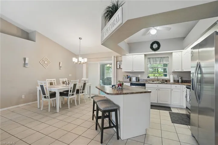 Kitchen featuring appliances with stainless steel finishes, a sink, dark countertops, light tile patterned floors, and lofted ceiling