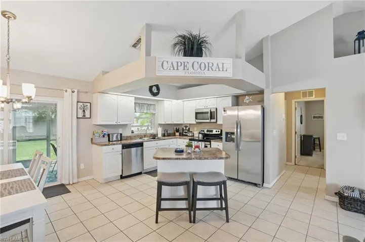Kitchen featuring appliances with stainless steel finishes, high vaulted ceiling, a chandelier, white cabinets, and light tile patterned floors