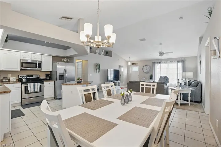 Dining room with light tile patterned flooring, a chandelier, a ceiling fan, baseboards, and lofted ceiling
