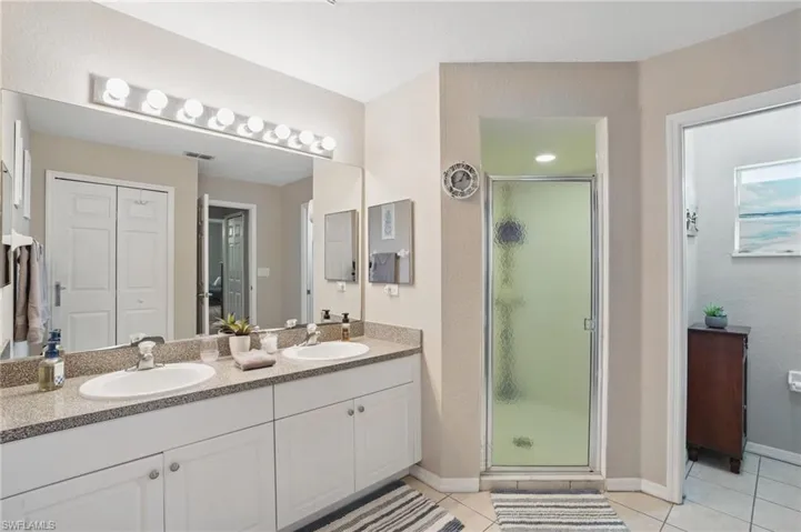 Full bath featuring a shower stall, tile patterned flooring, double vanity, and baseboards