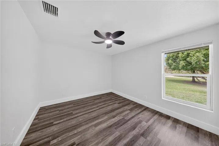 Bright interior space featuring a window with exterior scenery, dark wood-finish flooring, a ceiling fan with integrated lighting, white walls, and white baseboards