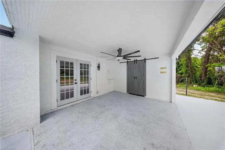 Covered patio featuring a ceiling fan, dual-pane French doors, a grey barn door, and a textured concrete floor