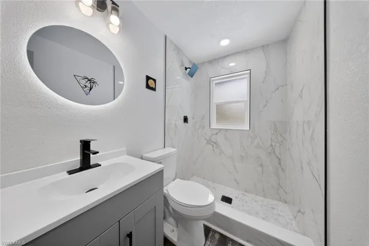 Bathroom featuring a contemporary vanity with an integrated sink, matte black faucet, and backlit oval mirror