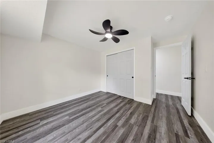 Room featuring wood-finish flooring, a contemporary ceiling fan, white bi-fold closet doors, and crisp white trim
