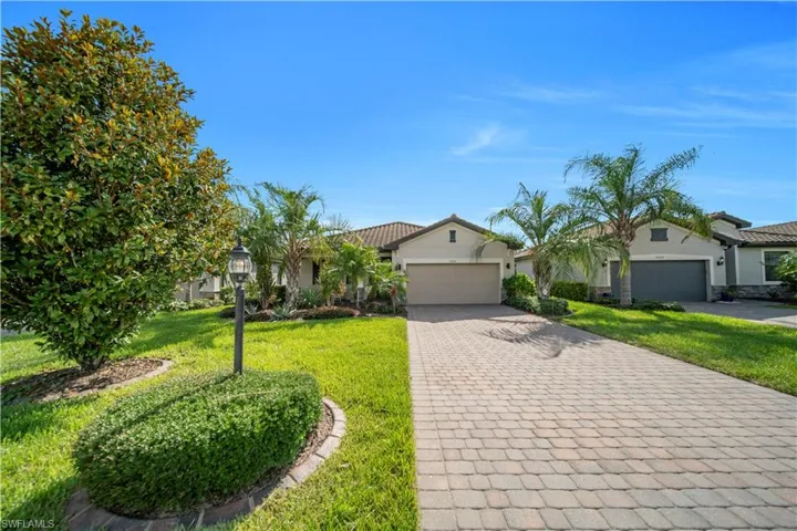 Contemporary stucco exterior featuring a paver driveway, mature landscaping, integrated garage, and a tiled roofline