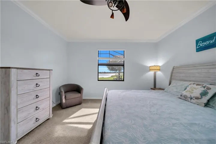Interior room featuring a window with water and landscape beyond, light blue walls with crown molding, and a ceiling fan with integrated lighting