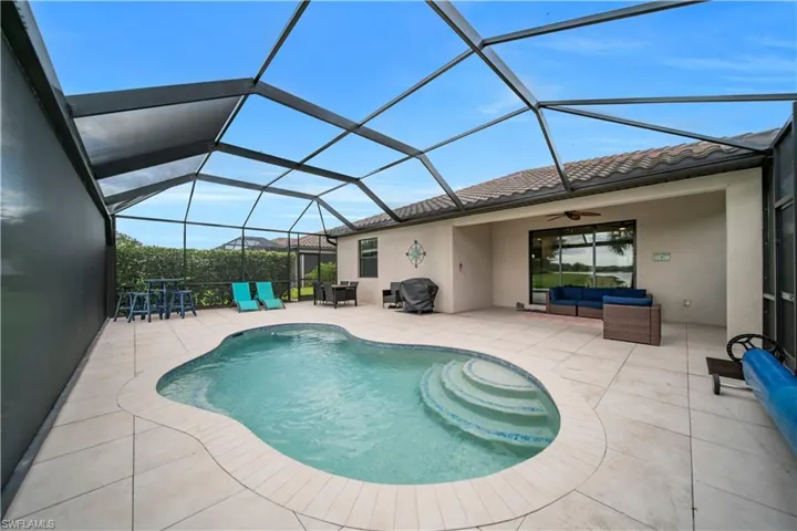 Screened outdoor living area featuring a freeform pool with steps, a spacious paver patio, and a tile roofline