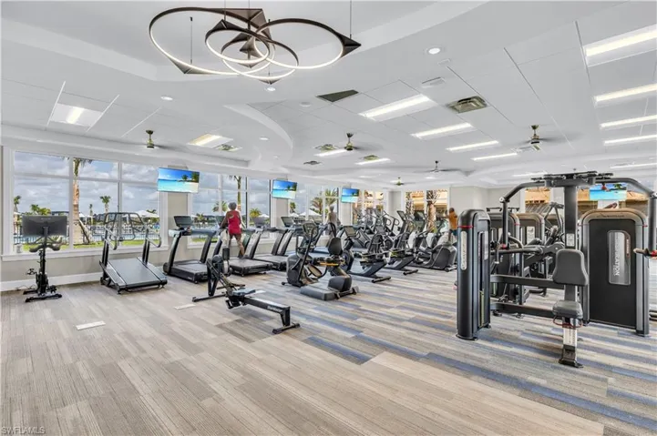 Exercise room featuring ceiling fan, a drop ceiling, and light colored carpet