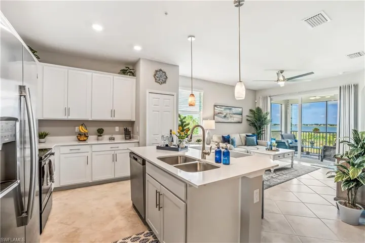 Kitchen with a center island with sink, white cabinetry, stainless steel appliances, sink, and decorative light fixtures