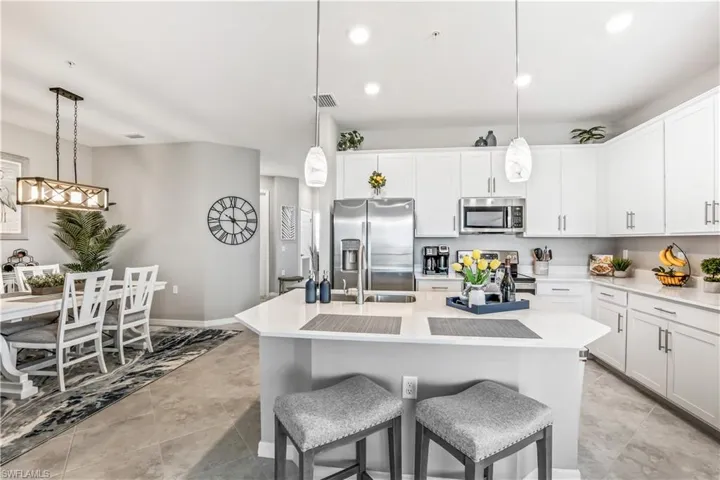 Kitchen featuring hanging light fixtures, a center island with sink, white cabinets, a kitchen bar, and appliances with stainless steel finishes
