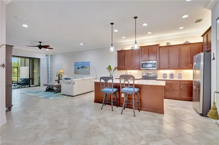 Kitchen featuring decorative light fixtures, ornamental molding, appliances with stainless steel finishes, ceiling fan, and a kitchen bar