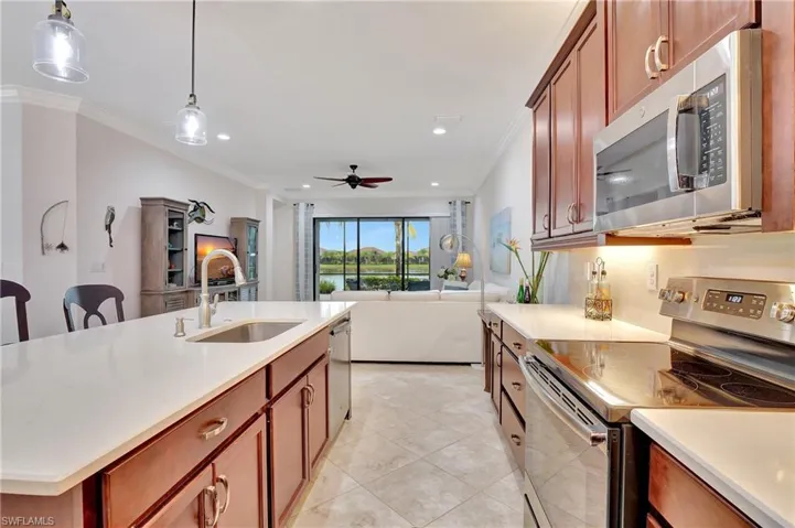 Kitchen featuring stainless steel appliances, hanging light fixtures, brown cabinetry, ornamental molding, and a center island with sink