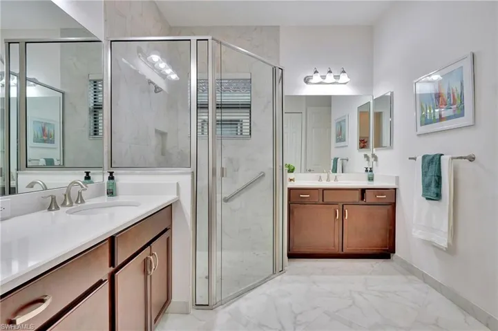 Bathroom with light marble finish flooring, two vanities, and a marble finish shower