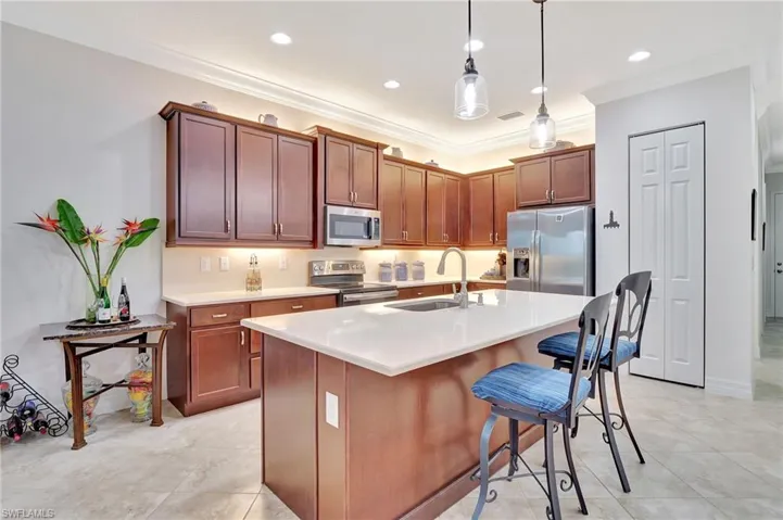 Kitchen with a breakfast bar, stainless steel appliances, a kitchen island with sink, decorative light fixtures, and light tile patterned floors