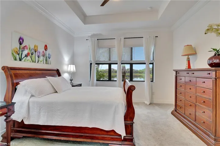 Bedroom with light colored carpet, a ceiling fan, crown molding, and a tray ceiling