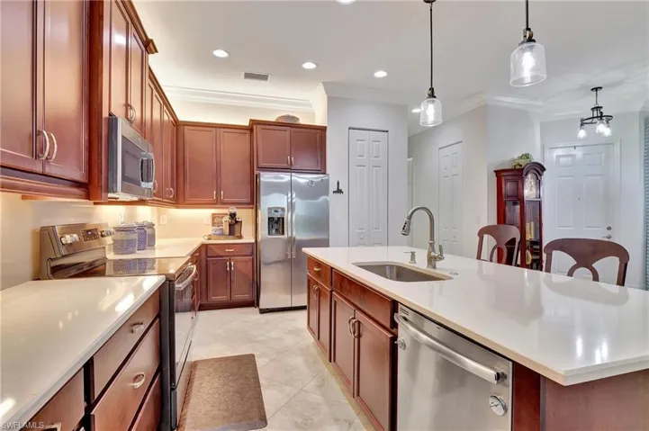 Kitchen featuring stainless steel appliances, pendant lighting, ornamental molding, a kitchen island with sink, and light stone counters