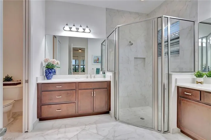 Bathroom with light marble finish flooring, a marble finish shower, and vanity