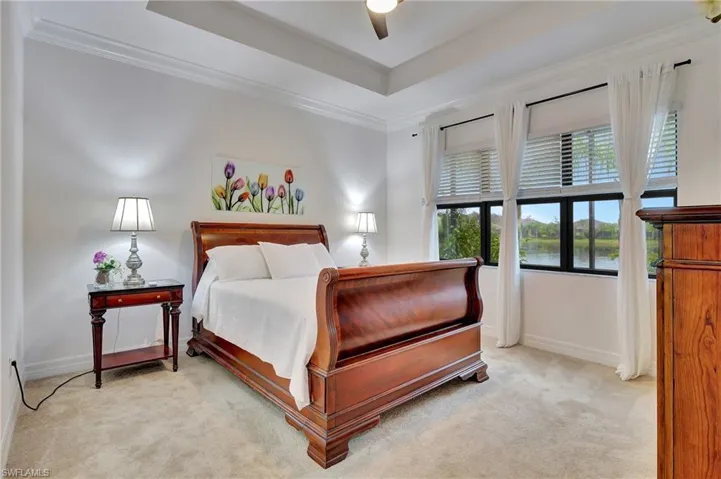 Bedroom with light carpet, ornamental molding, a tray ceiling, and a ceiling fan