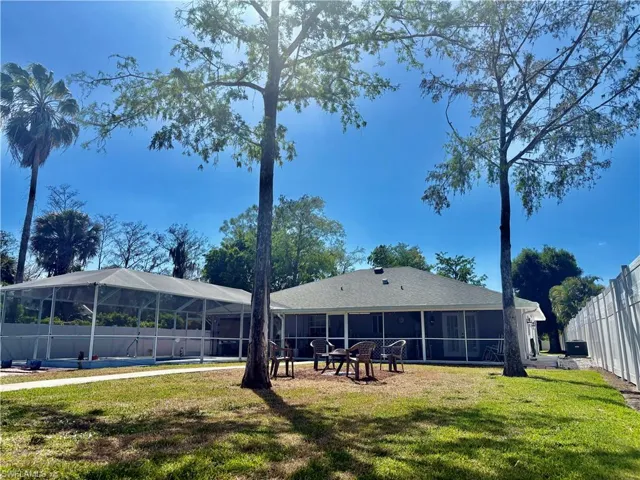 Rear view of house featuring a sunroom, glass enclosure, fence, and a lawn