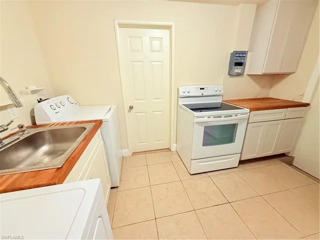 2nd Kitchen featuring range, washer / dryer, light tile patterned floors, white cabinets, and butcher block counters