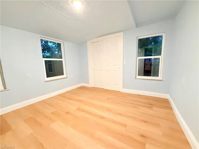Unfurnished bedroom featuring light wood-type flooring, a textured ceiling, a closet, and lofted ceiling