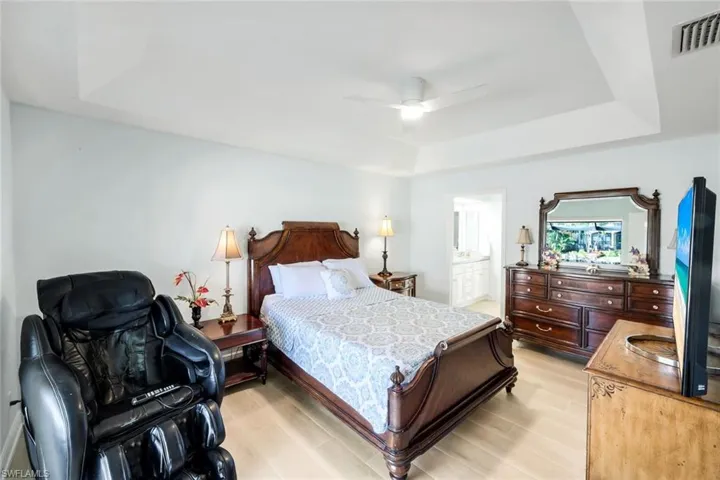 Bedroom with a raised ceiling, light wood-style floors, a ceiling fan, and ensuite bathroom