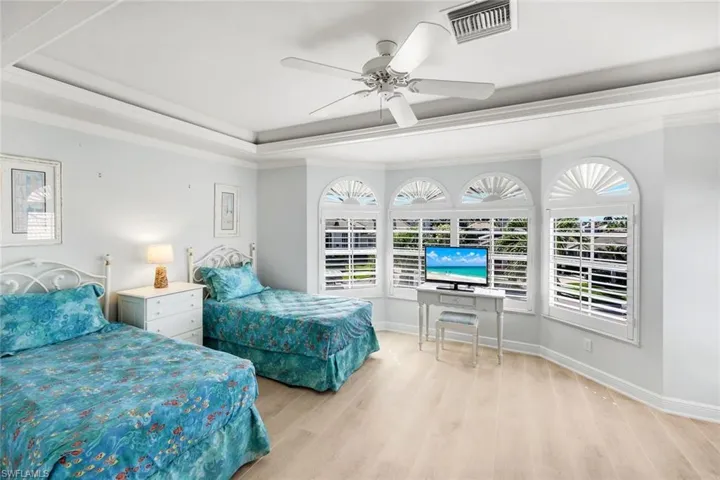 Bedroom featuring crown molding, a tray ceiling, light wood-type flooring, and a ceiling fan