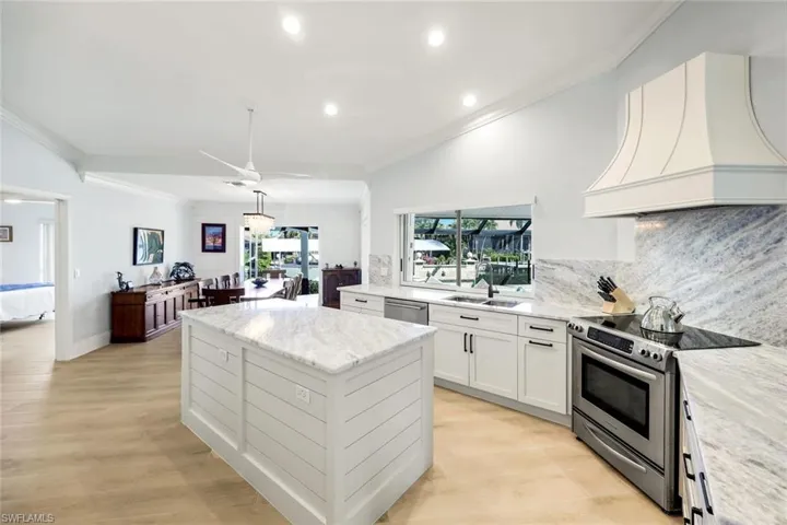 Kitchen with white cabinets, stainless steel appliances, custom range hood, a center island, and ornamental molding