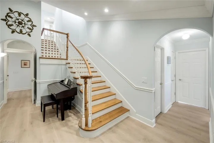 Stairs featuring arched walkways, wood finished floors, and ornamental molding