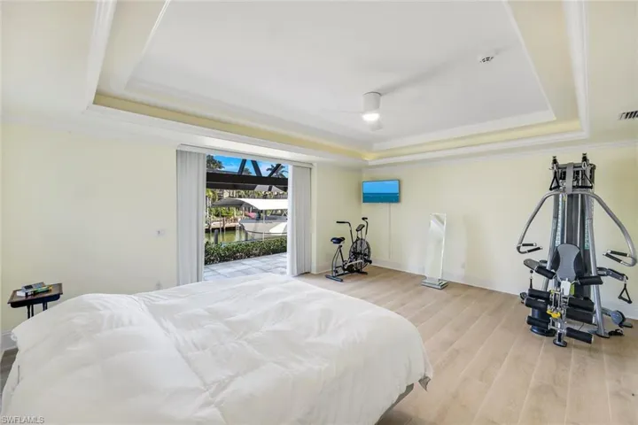 Bedroom with a tray ceiling, ornamental molding, access to exterior, ceiling fan, and wood finished floors