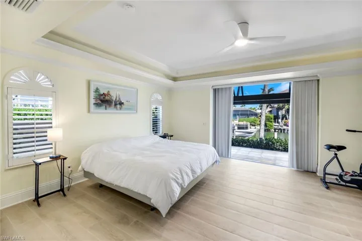 Bedroom with a water view, ornamental molding, light wood-style flooring, a tray ceiling, and access to exterior