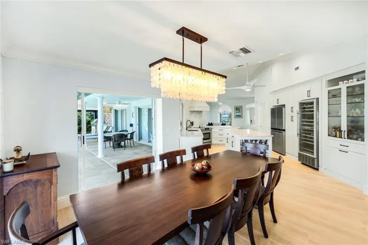 Dining space featuring beverage cooler, healthy amount of natural light, ornamental molding, a chandelier, and light wood finished floors