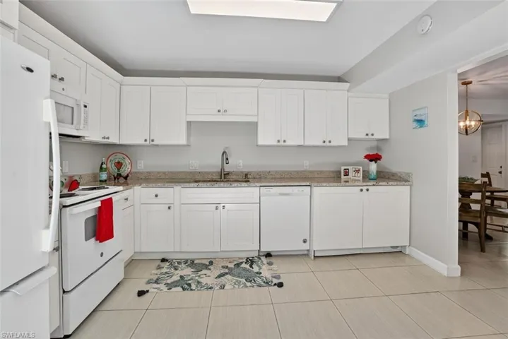 Kitchen with white appliances, white cabinetry, suspended lighting, and granite counter tops