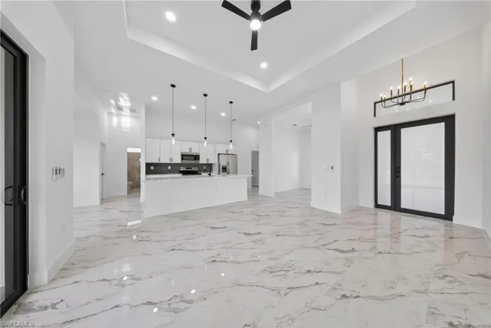 Unfurnished living room with suspended lighting, a ceiling fan, a tray ceiling, and light marble finish floors