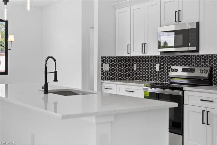 Kitchen featuring stainless steel appliances, light stone counters, white cabinetry, a center island with sink, and decorative backsplash