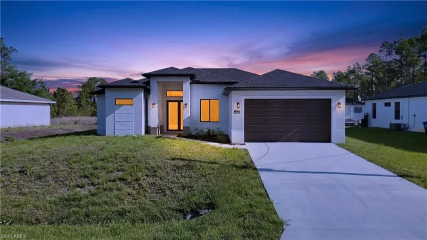 Prairie-style home featuring a lawn, stucco siding, an attached garage, concrete driveway, and roof with shingles
