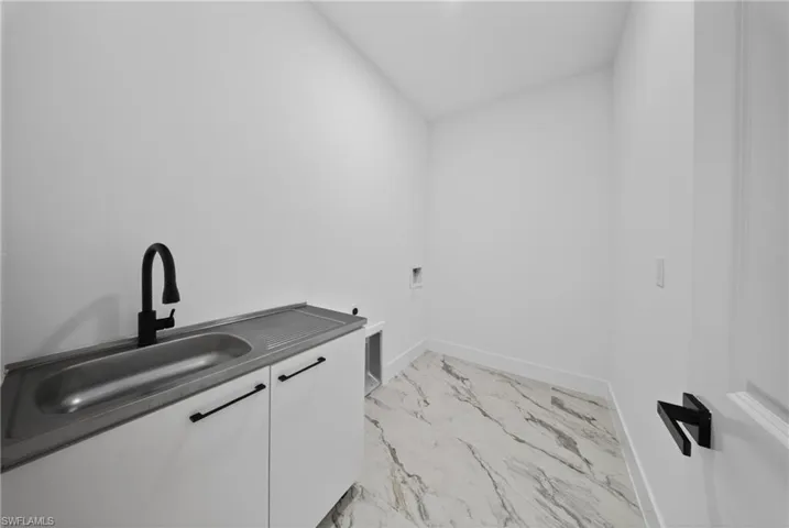 Laundry area with washer hookup, cabinet space, light marble finish flooring, and vaulted ceiling