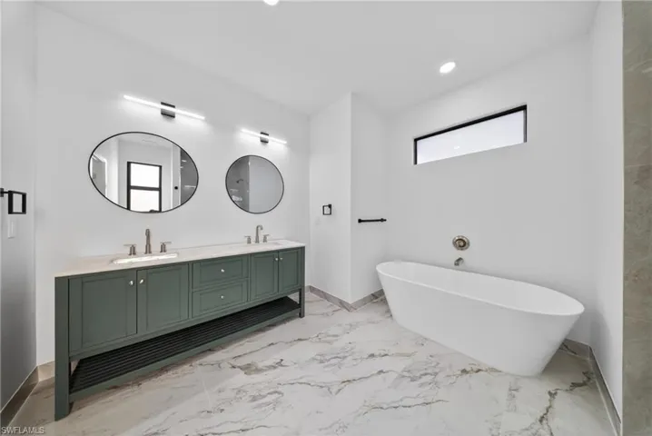 Bathroom with double vanity, light marble finish floors, a freestanding tub, and recessed lighting