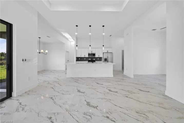 Unfurnished living room featuring suspended lighting, a tray ceiling, and light marble finish flooring