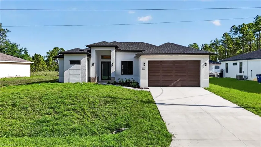 Prairie-style home featuring a front yard, stucco siding, a garage, and driveway