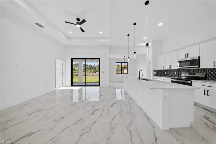 Kitchen featuring white cabinetry, stainless steel appliances, a kitchen island with sink, open floor plan, and a ceiling fan