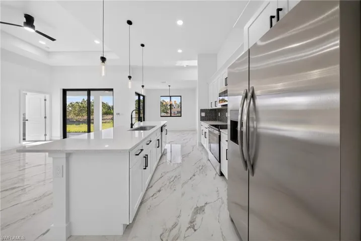 Kitchen with stainless steel appliances, white cabinetry, a large island with sink, light stone counters, and a ceiling fan
