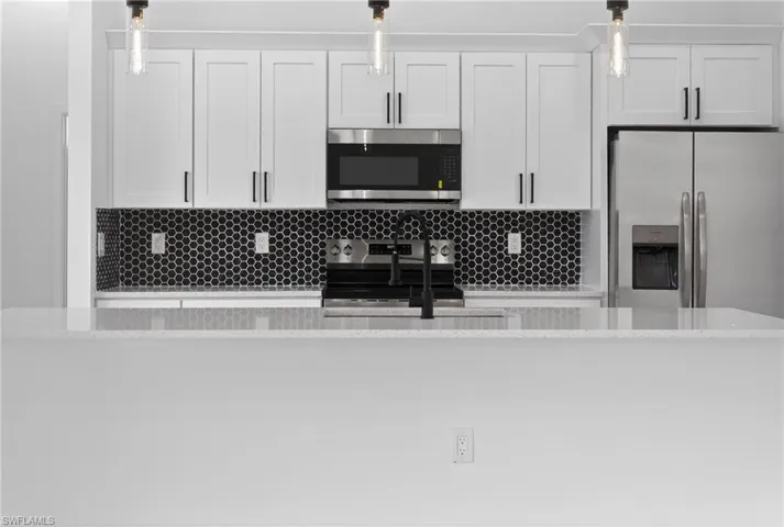 Kitchen featuring decorative light fixtures, stainless steel appliances, light stone counters, white cabinets, and an island with sink